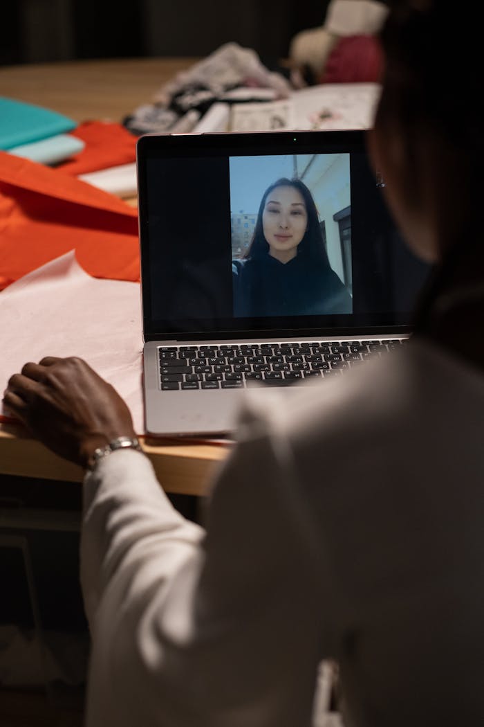 A woman in a creative workspace on a video call with a colleague on a laptop.